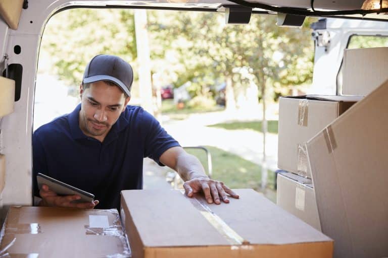 Courier With Digital Tablet Checking Packages In Van